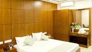 A modern bedroom with a wooden bed, bedside tables, a nightstand, a desk with a mirror, and a ceiling fan. - Shoba Inn (Bengaluru)
