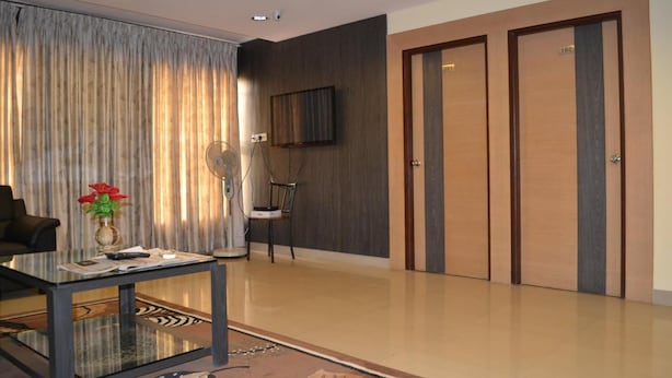 A modern hotel lobby with a glass coffee table, a chair, a television mounted on the wall, and a pair of wooden doors. - Shoba Inn (Bengaluru)