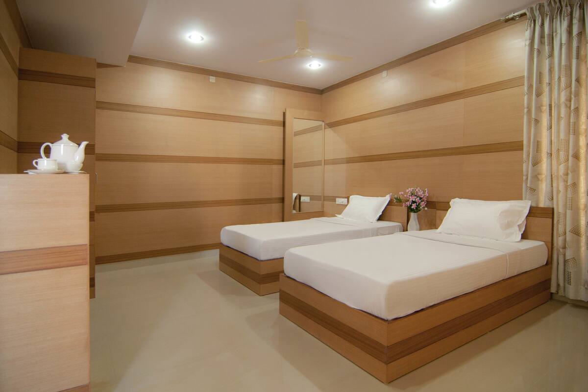 A hotel room with two single beds, a wooden headboard, a ceiling fan, and a bedside table with a white teapot and cup.