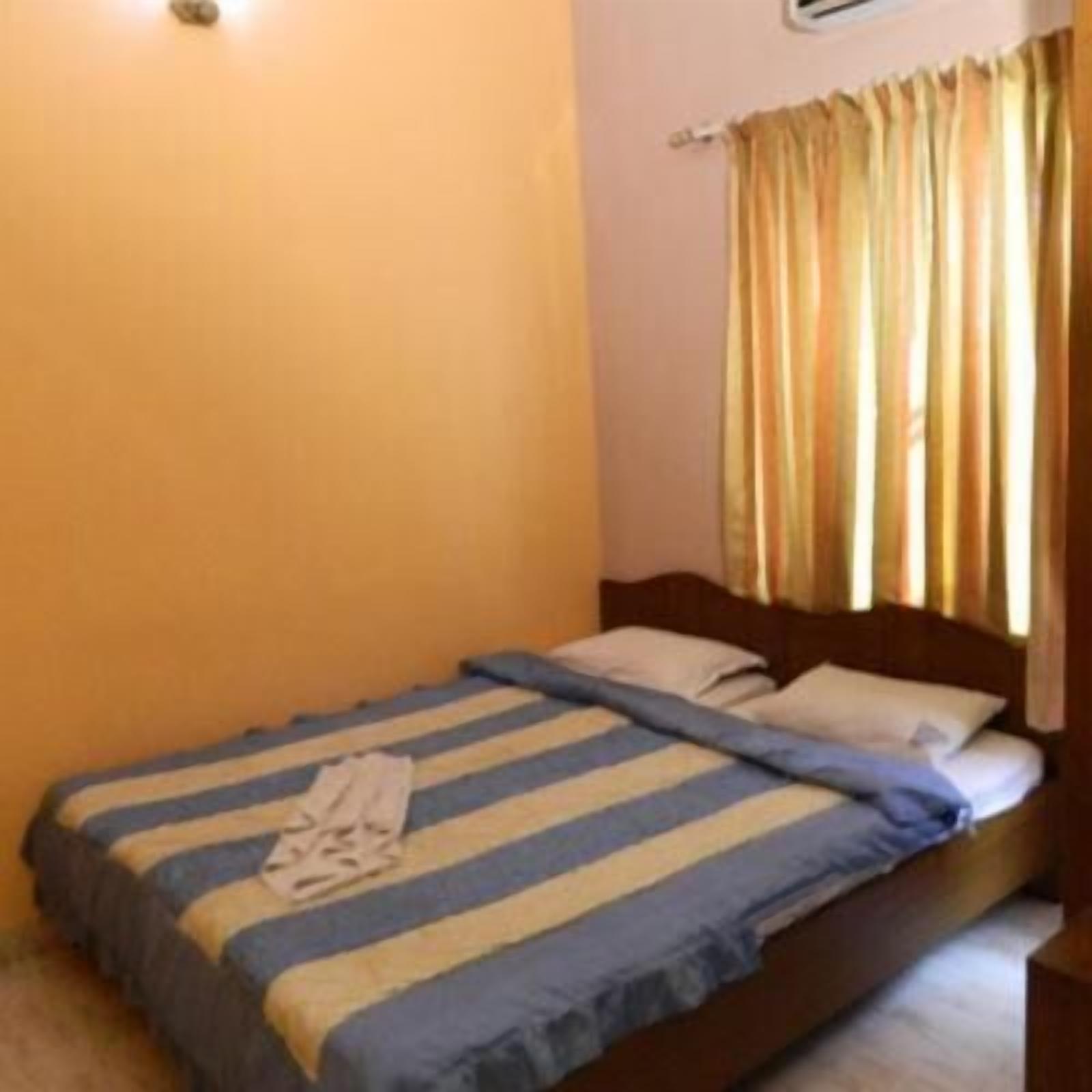 A single bed with a striped bedspread, a wooden headboard, and a window with curtains.