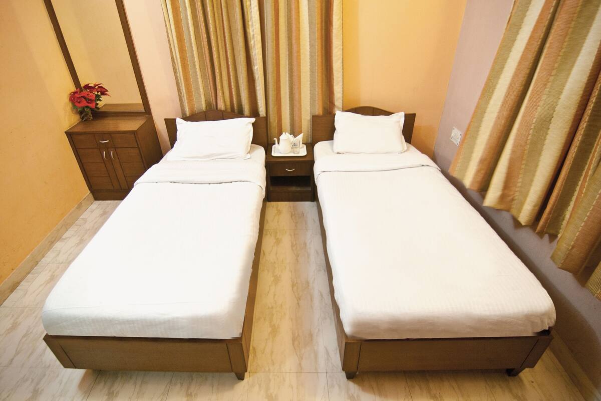 A double room with two single beds, a small wooden cabinet, a nightstand with a tray, and a curtain.
