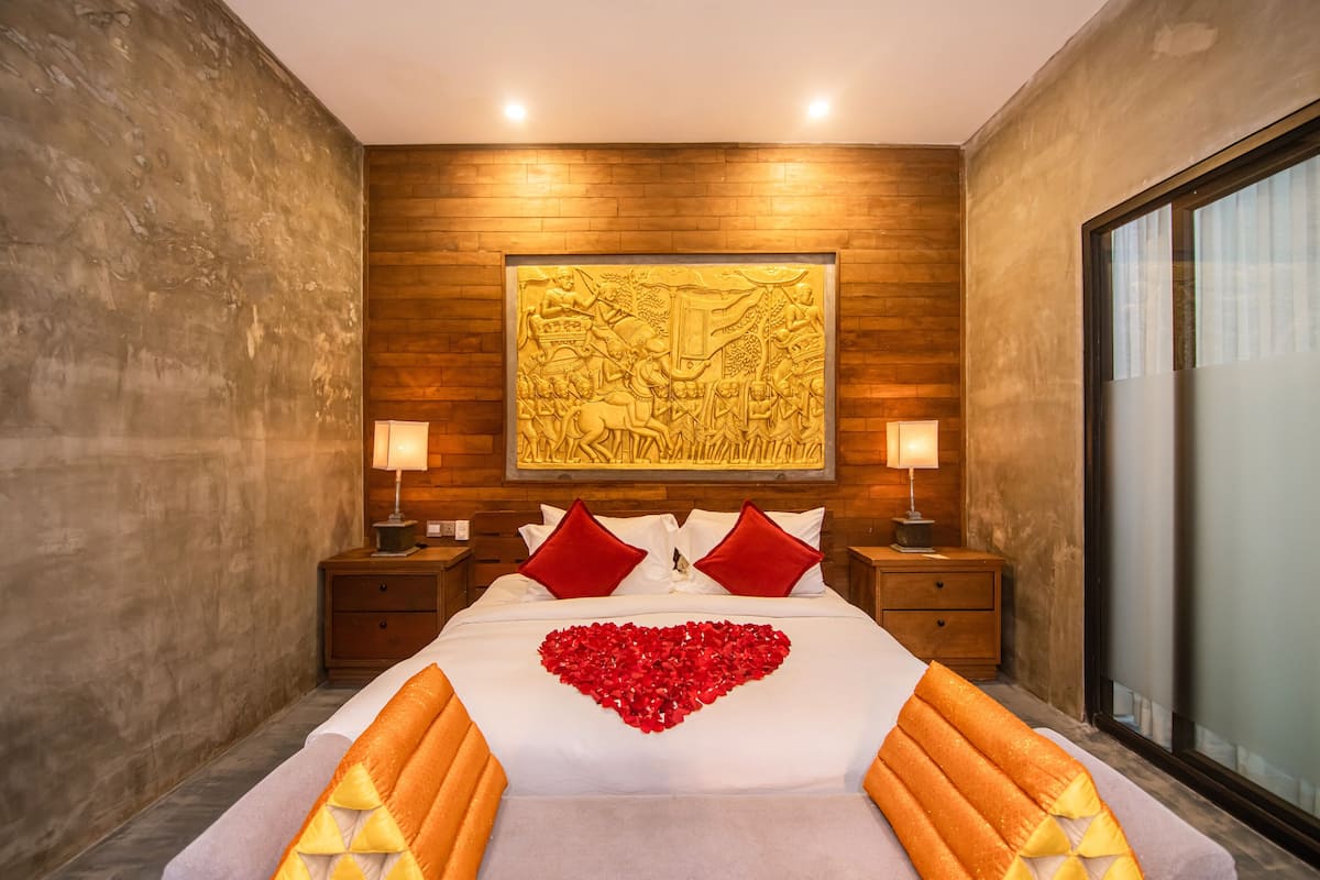 A modern hotel room with a large bed, wooden paneling on the walls, and a decorative relief above the bed.