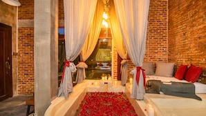 A romantic setting with a bathtub filled with rose petals, candles, and a cozy seating area with a view of a brick wall and a window. - Cambana d'Angkor Suites (Siem Reap)