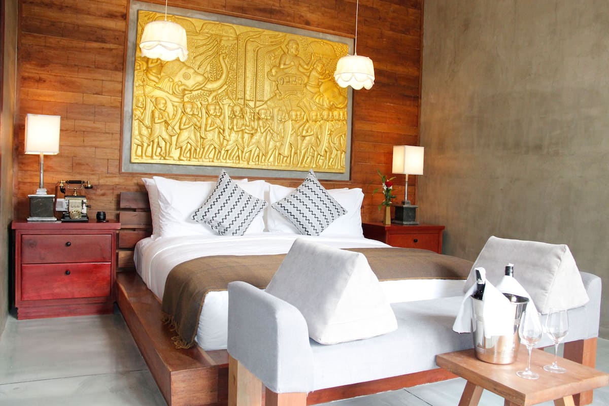 A modern hotel room with a large bed, two nightstands, a wooden headboard, and a large wall mural.