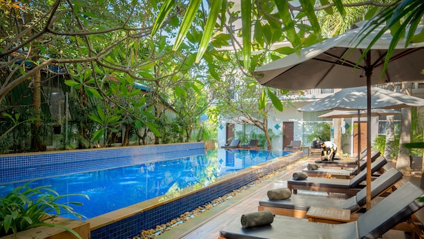 A pool area with lounge chairs and umbrellas, surrounded by lush greenery. - Landing Gold By Amatak (Siem Reap)