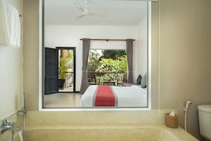Ein Hotelzimmer mit einem großen Bett, einem Badezimmer mit einer Badewanne und Blick auf einen Balkon mit Pflanzen.