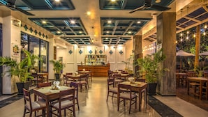 A restaurant with wooden tables and chairs, a bar area, and potted plants. - Landing Gold By Amatak (Siem Reap)