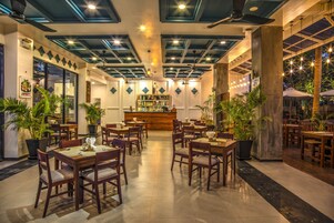 Un restaurante con mesas y sillas de madera, una zona de bar y plantas en macetas.