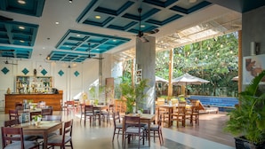 A spacious indoor area with multiple dining tables and chairs, a bar area with a variety of bottles, and a view of a pool area with umbrellas. - Landing Gold By Amatak (Siem Reap)