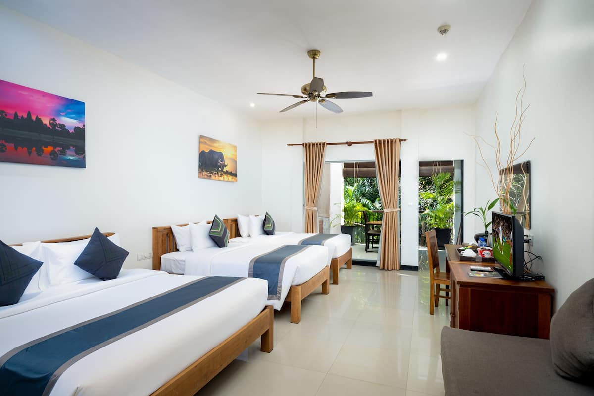 Une chambre d’hôtel avec trois lits, un ventilateur de plafond, un bureau avec une télévision et une vue sur la verdure.