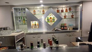 Zona de bar con estantes llenos de botellas de licores y vasos.