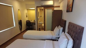 Habitación de hotel con dos camas, un escritorio y un baño visible a través de una puerta abierta.