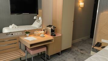 A hotel room with a bed, a desk with a computer, a TV, and a bedside table with a lamp and a phone.