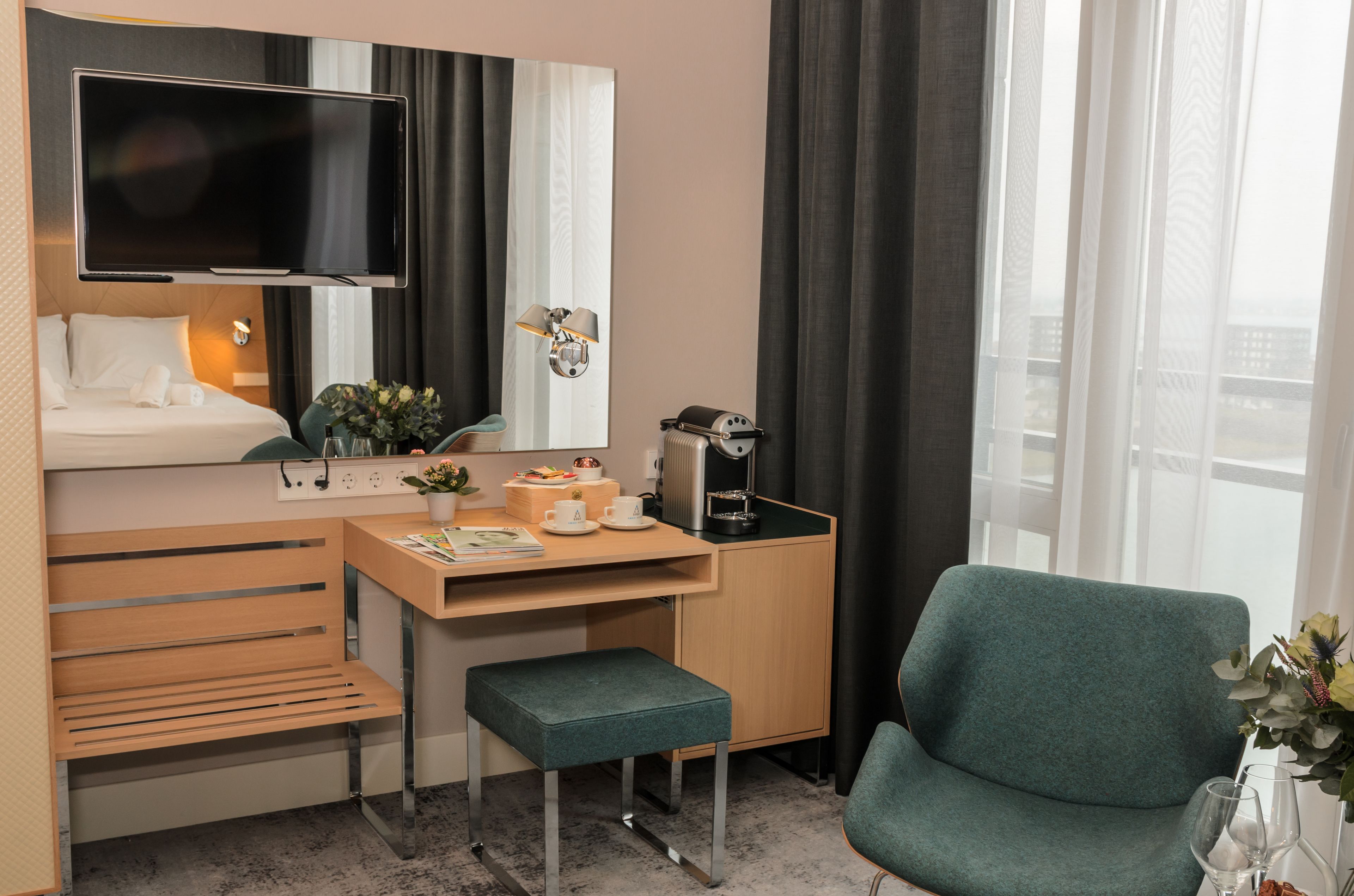A hotel room with a bed, a desk with a computer, a chair, a TV, and a window with curtains.