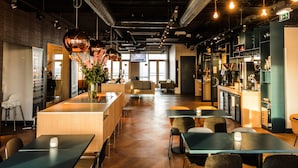 Un restaurante moderno con barra, mesas y sillas de madera. Se observa un mostrador de recepción y un ventanal grande al fondo.