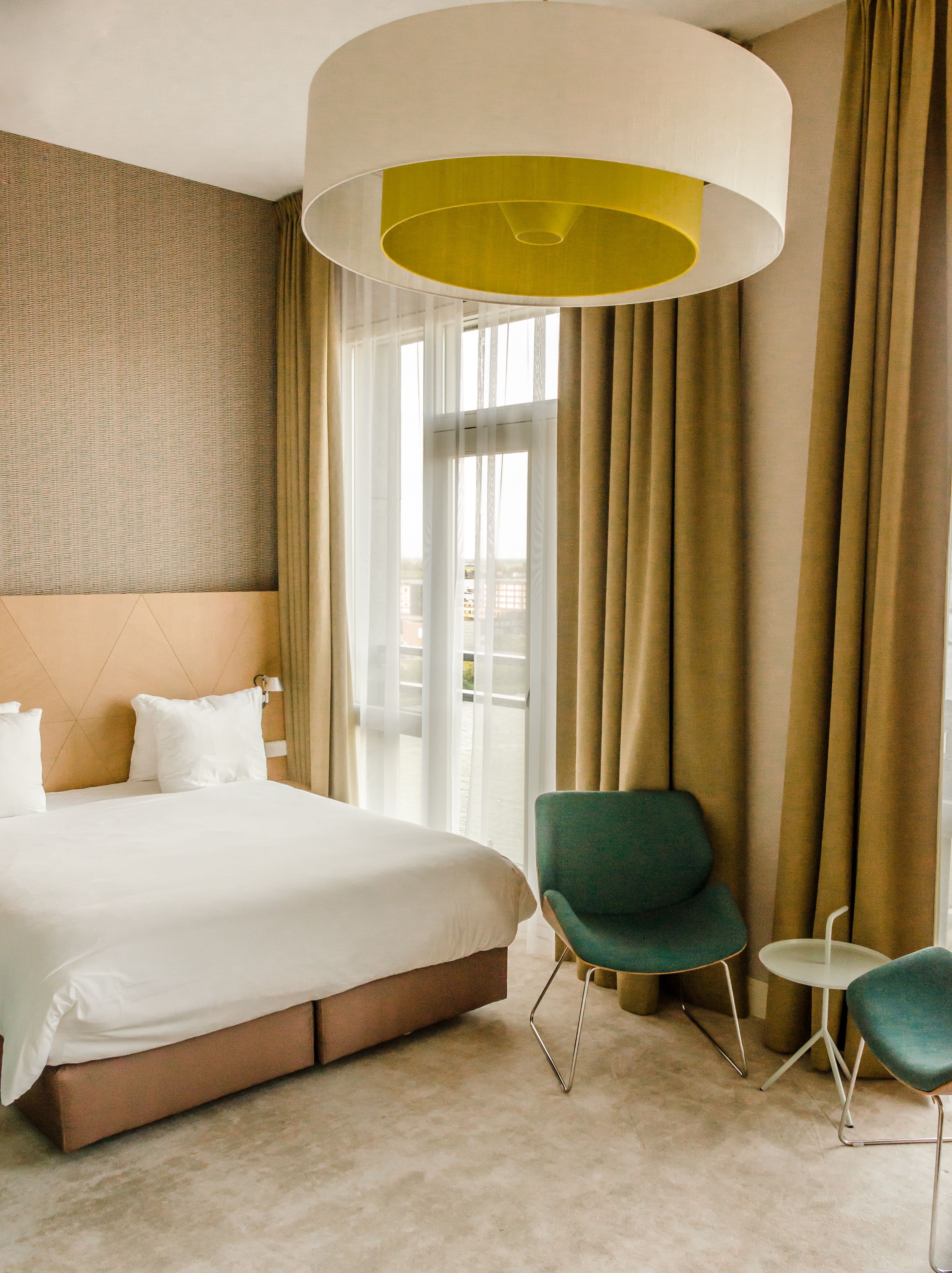 Ett hotellrum med en stor säng, en grön fåtölj, ett litet bord och en modern taklampa.
