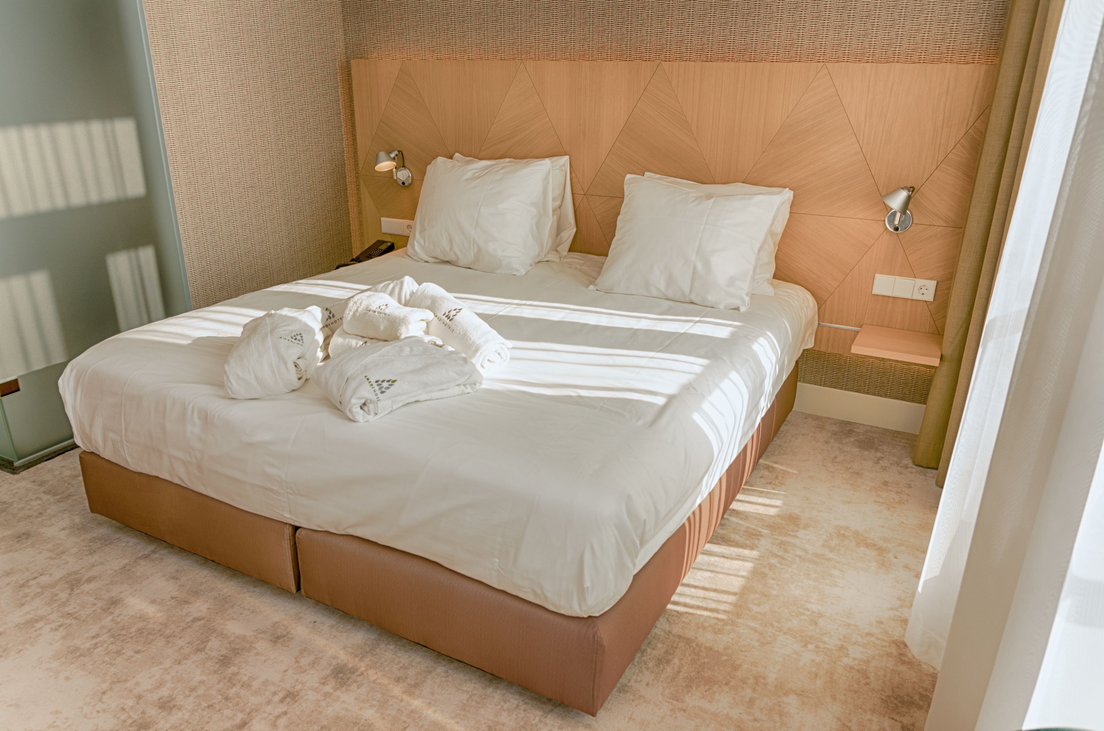 A neatly made bed with white linens and towels, a wooden headboard, and a bedside table with a lamp.