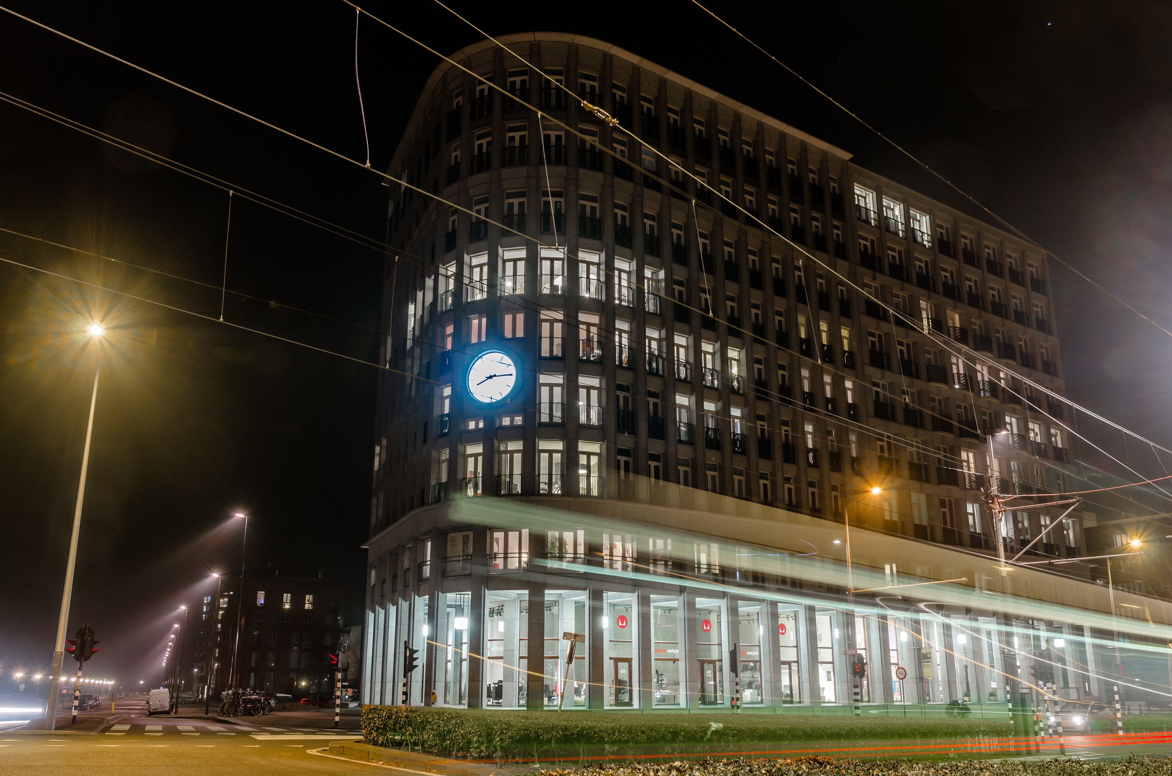 Ein modernes Gebäude mit einer markanten Uhr an der Fassade, mehreren Etagen und einem Glasvorbau.