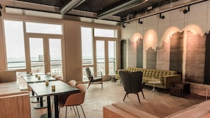 Un espacio de oficina moderno con ventanas amplias, un sofá verde y una zona de comedor con mesas y sillas.
