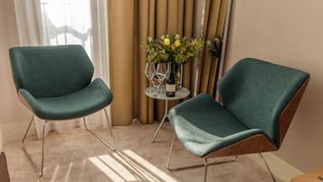 Two teal armchairs with metal legs, a small round table with a vase of flowers, and a window with curtains.
