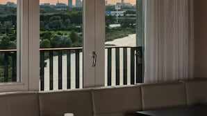 Habitación con vista a un horizonte urbano al atardecer, un balcón con barandilla y una mesa con una silla.