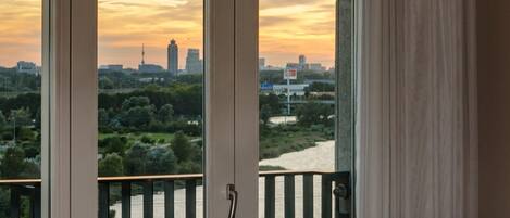 Habitación con vista a un horizonte urbano al atardecer, un balcón con barandilla y una mesa con una silla.