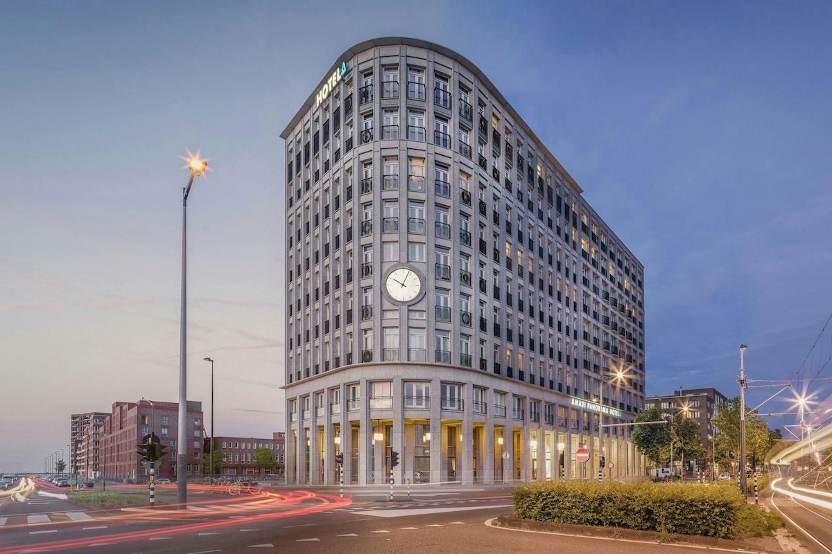 A multi-story hotel with a prominent clock on the facade, located at a city intersection with visible traffic.