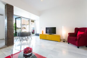 A modern living room with a glass coffee table, a red armchair, a yellow TV stand, and a large window offering a view of the outdoors.