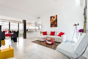 A modern living room with a white sofa, red cushions, a glass coffee table, and a yellow side table.