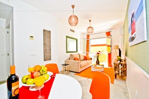 A modern living room with a sofa, a dining table with fruit and wine, and a kitchen area visible in the background. - The Zentral Suites & Apartments (Seville)