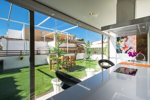 A modern kitchen with a large window, a dining area with a table and chairs, and a view of a garden and neighboring buildings. - The Zentral Suites & Apartments (Seville)
