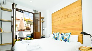 Une chambre d’hôtel avec un lit, une tête de lit en bois, une table de chevet, une lampe et une vue sur le balcon extérieur.