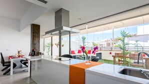 Une cuisine moderne dotée d’un grand îlot central, d’un coin repas avec des chaises et une table, et offrant une vue sur la ville grâce à de grandes fenêtres.