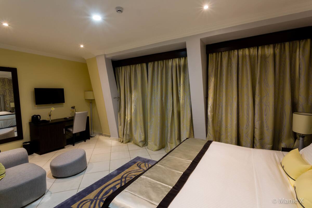 A hotel room with a large bed, a desk, a chair, a TV, and curtains.