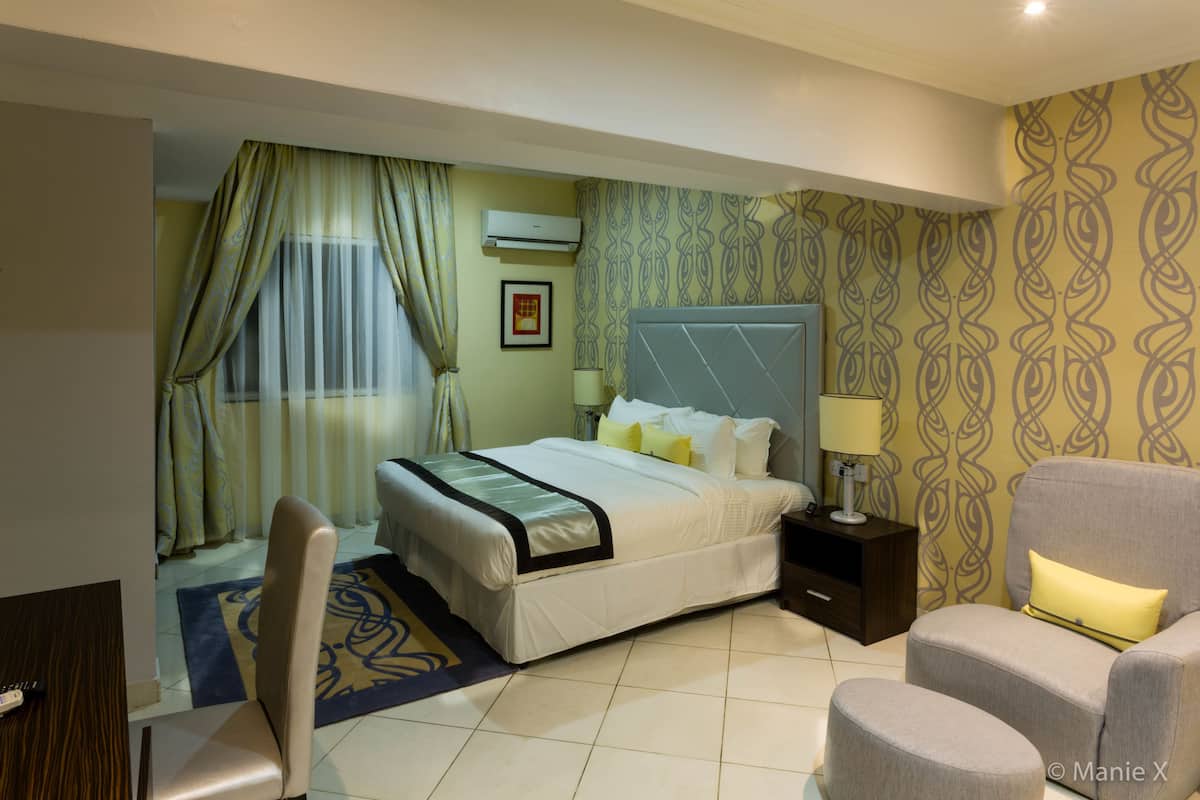 A hotel room with a bed, a chair, a nightstand, and a desk.