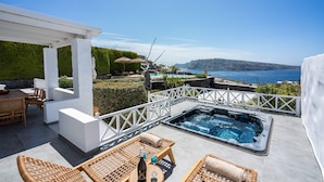 A rooftop pool area with a hot tub, lounge chairs, and a table with a bottle and glass.