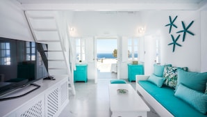 A modern living room with a TV, teal furniture, and a view of the sea.