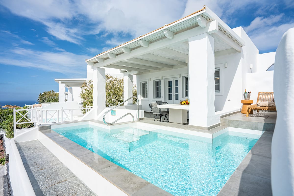 A white villa with a swimming pool, outdoor seating, and a view of the sea.