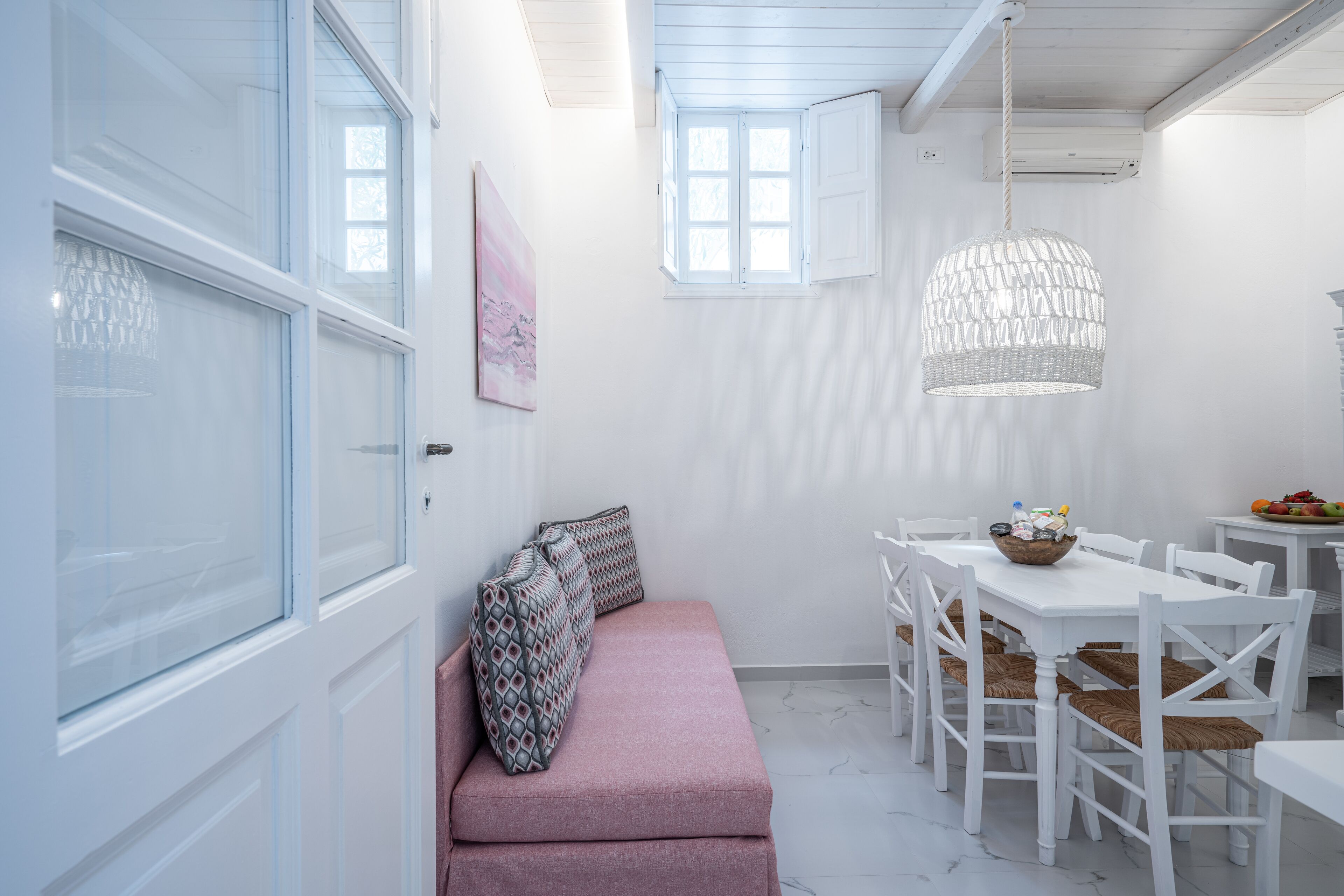 Un interior en tonos blancos con un banco rosa, una mesa de comedor blanca y sillas.