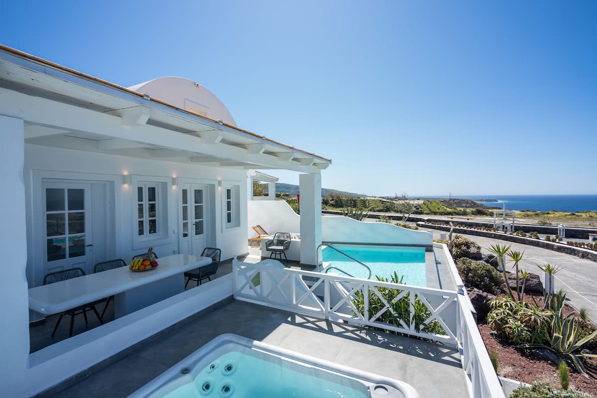 A modern outdoor pool area with a hot tub, a dining table with chairs, and a view of the ocean.