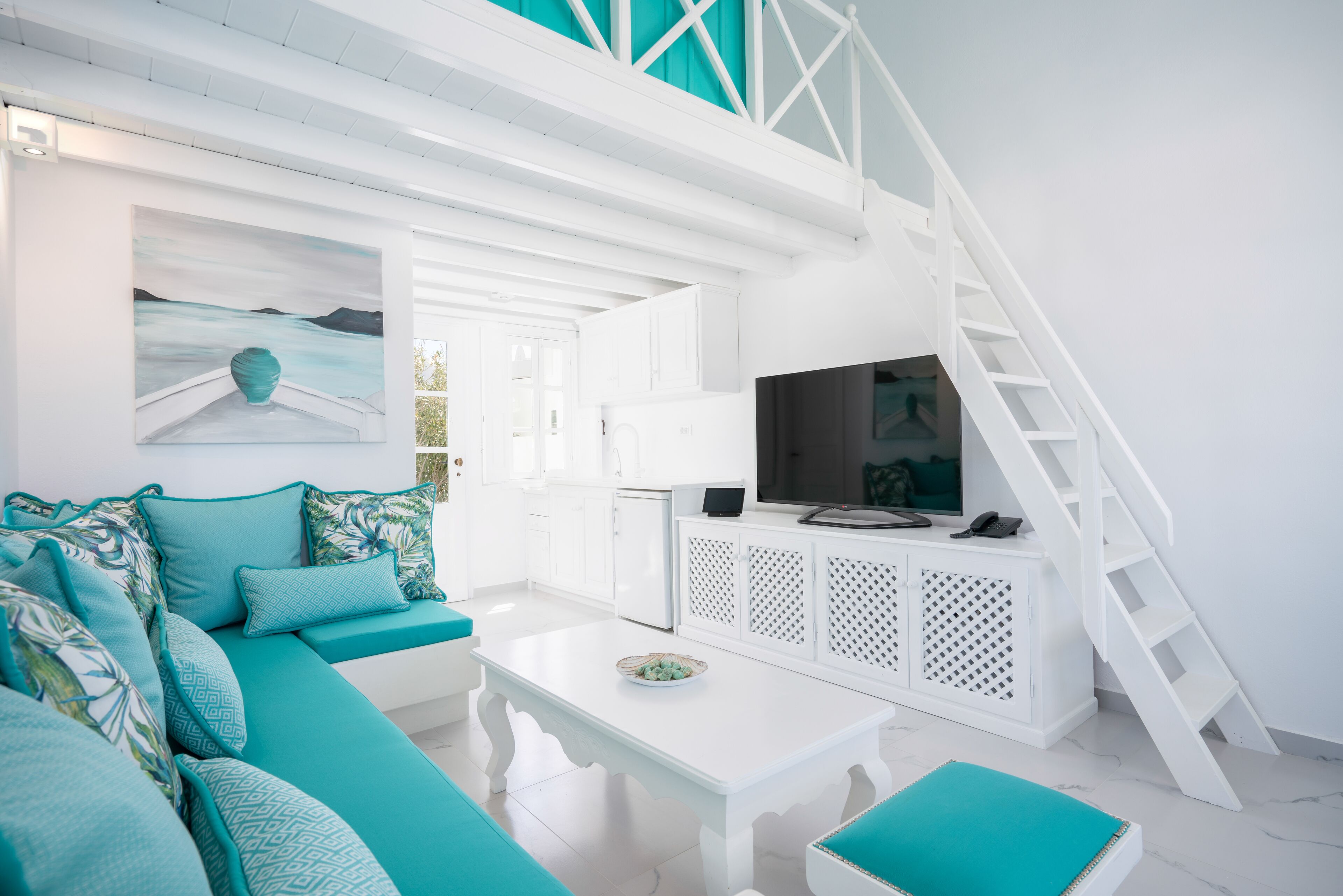 A modern living room with a teal sofa, white coffee table, and a TV on a white cabinet.