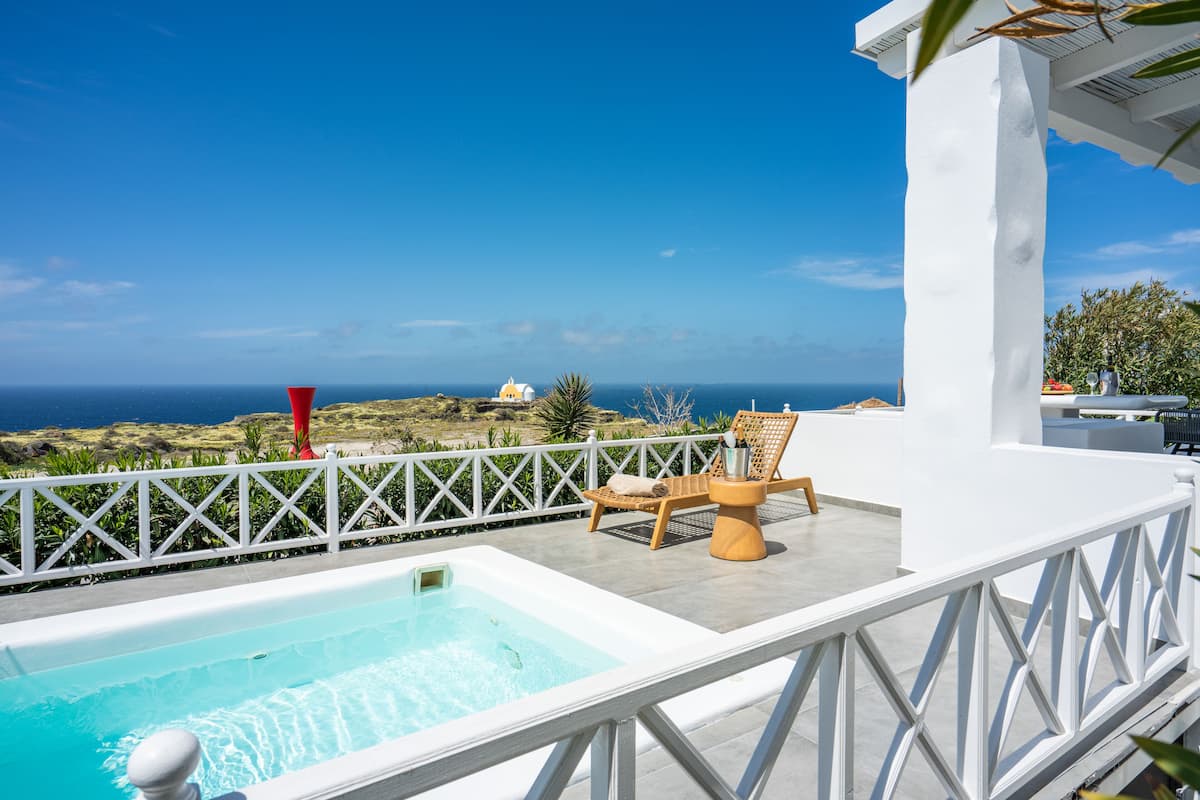 A rooftop pool area with a view of the ocean, white railings, and a wooden chair.