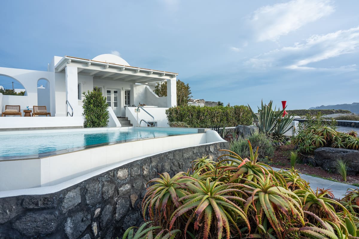 A modern white building with a pool, outdoor seating, and a view of the sea.