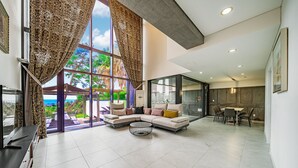 A modern living room with a large window, a sofa, a coffee table, and a dining area with chairs. - Dam & Roo (Seogwipo)