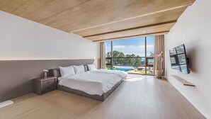A modern bedroom with a large bed, a nightstand, a TV mounted on the wall, and a view of a swimming pool through large windows. - Dam & Roo (Seogwipo)