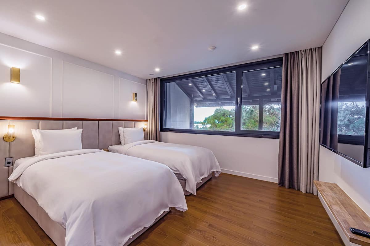 A hotel room with two beds, a large window, a TV, and a wooden floor.