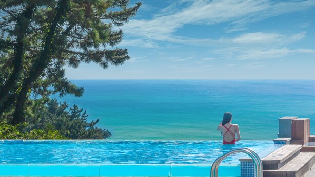 A pool with a view of the ocean, surrounded by trees. - Dam & Roo (Seogwipo)