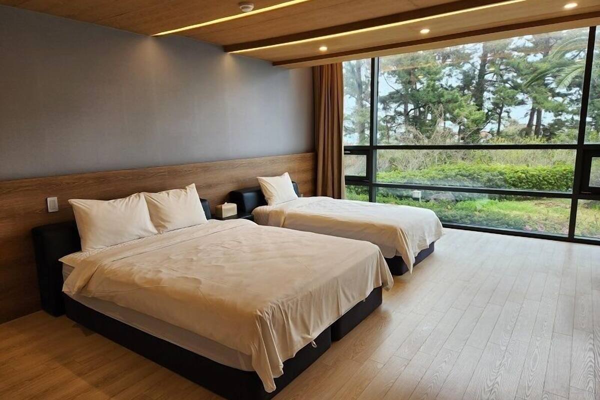 A hotel room with two beds, a large window, and a view of trees.