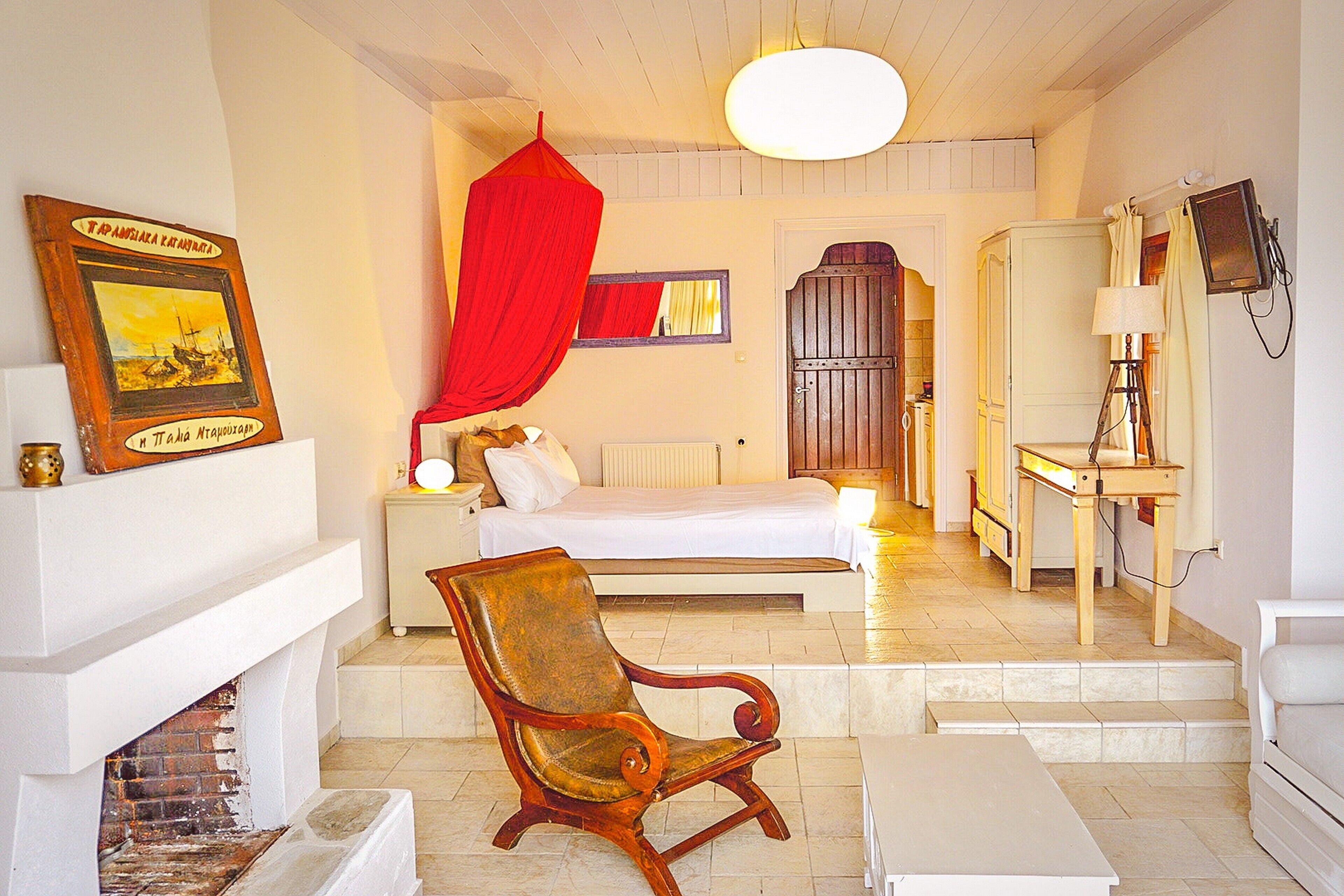 A room with a bed, a wooden chair, a desk with a lamp, and a fireplace.