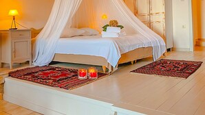 A bedroom with a canopy bed, bedside lamps, a nightstand, and a red patterned rug. - Palia Damouchari (Zagora-Mouresi)